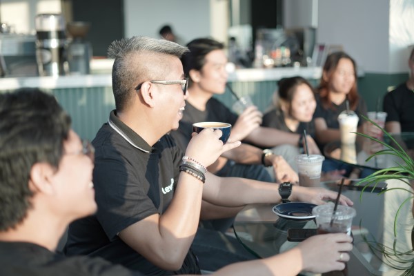 A LevelUp team member smiling and holding a coffee cup during a casual group discussion around a glass table.