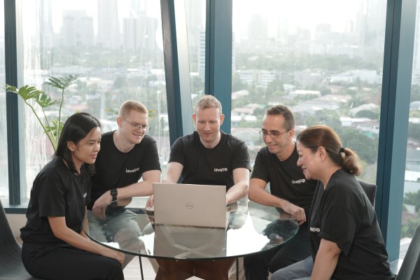 LevelUp team members gathered around a laptop, brainstorming together in a bright office space with large windows overlooking a cityscape.