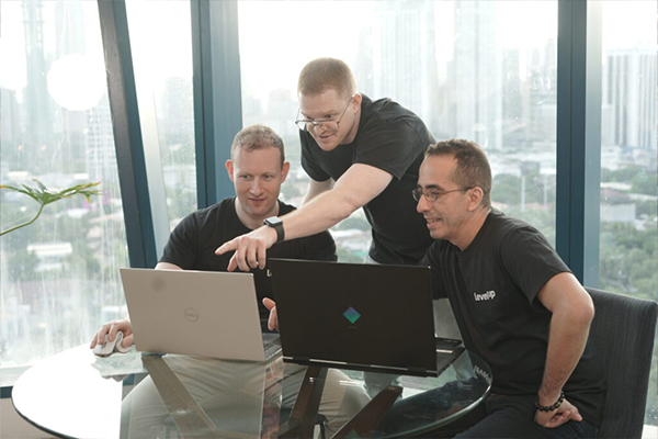 LevelUp team members gathered around two laptops, collaborating and pointing at the screens with a cityscape visible through large windows.